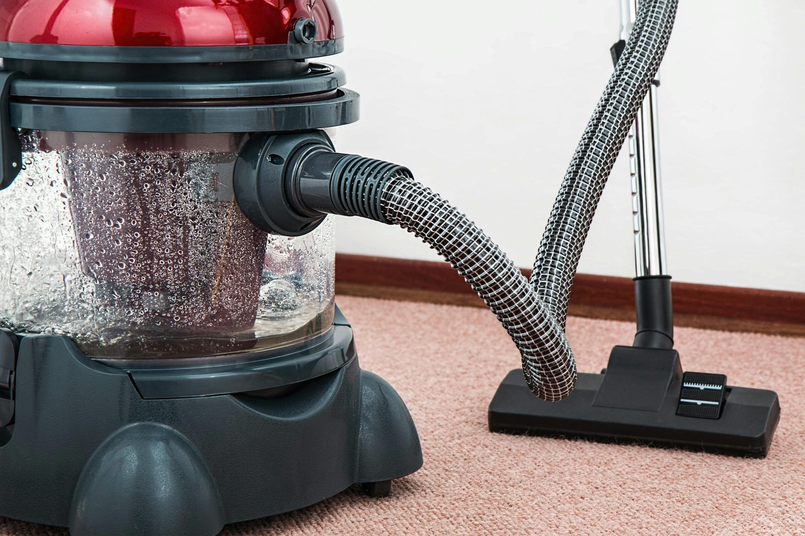 Woman vacuuming living room carpet with vacuum cleaner, modern kitchen and sofa in background